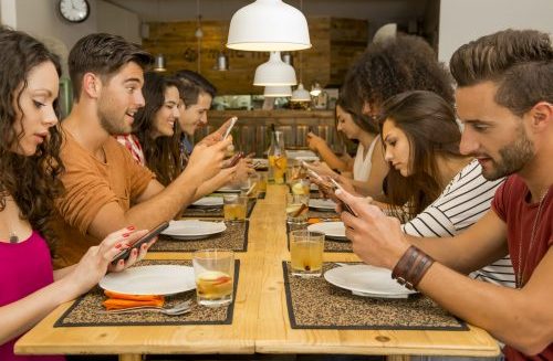 Viele junge Leute sitzen zusammen am Tisch, sind aber nicht zusammen, sondern mit ihrem Handy beschäftigt