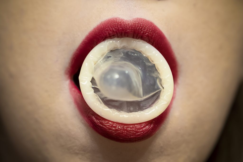 Erster Schritt, um ein Kondom mit dem Mund überzuziehen: Zwischen die Lippen nehmen